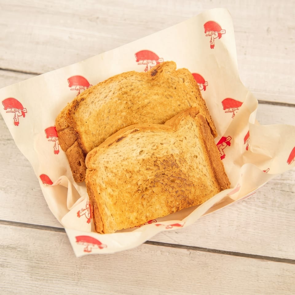 Two slices of golden-brown toast in a paper-lined basket on a light wooden table.