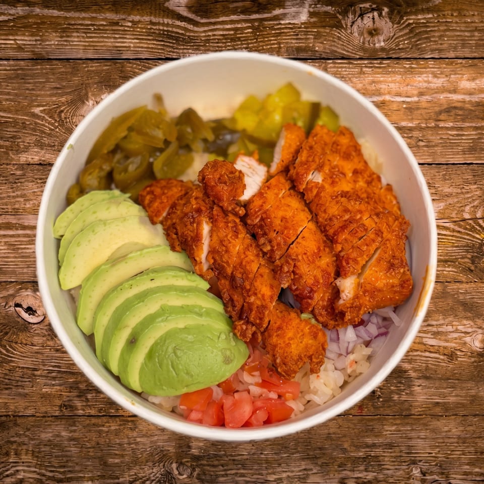 Crispy chicken, sliced avocado, pickled jalapeños, and diced tomatoes over rice in a white bowl.