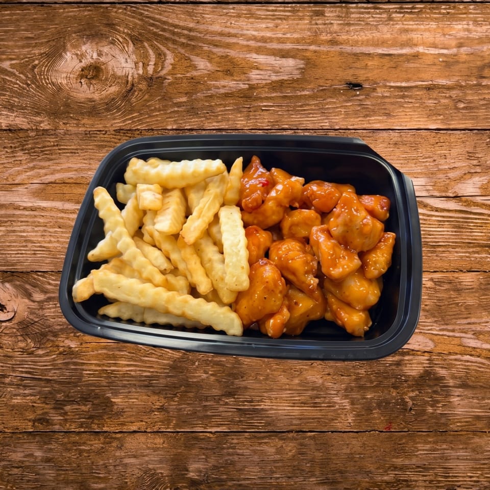 Black takeout container with crinkle-cut fries and orange chicken on a wooden table.