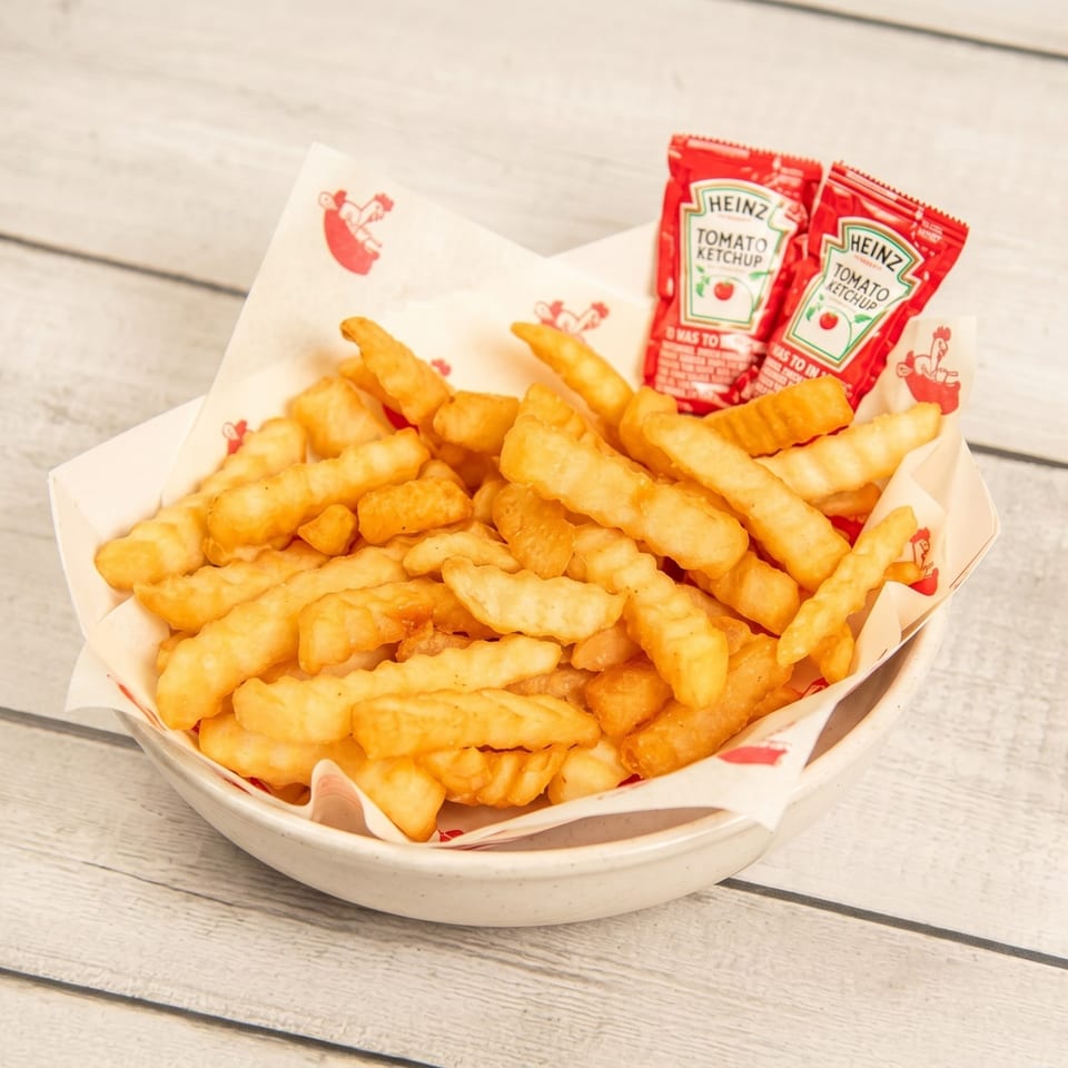 A white bowl filled with golden crinkle-cut fries and two Heinz ketchup packets on a wooden table.