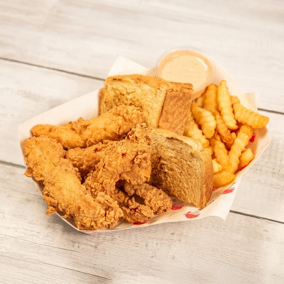 Crispy fried chicken tenders, crinkle-cut fries, Texas toast, and dipping sauce in a paper basket.