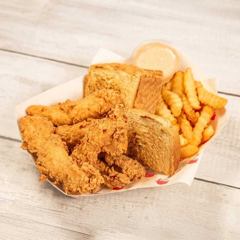 Crispy fried chicken tenders, crinkle-cut fries, Texas toast, and dipping sauce in a paper basket.