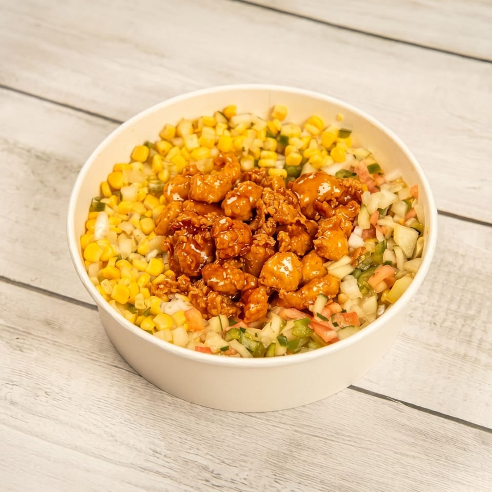 A white bowl filled with golden popcorn chicken, corn, and diced vegetables on a wooden surface.